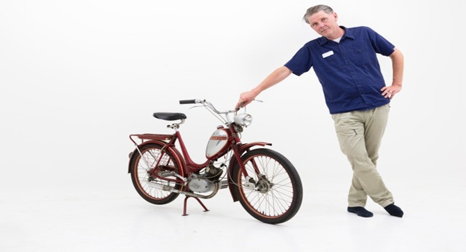 Claes Johansson står lutad mot en moped.