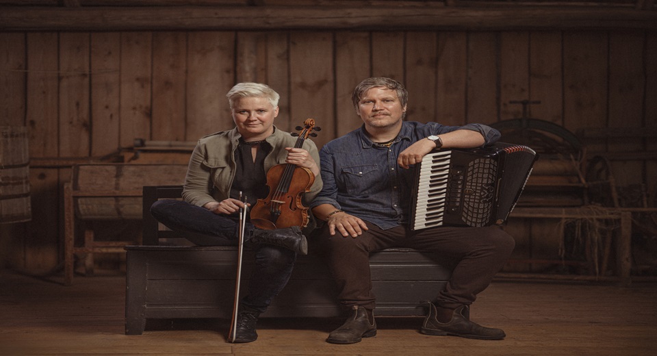 En man och en kvinna sitter med var sitt instrument i knät.