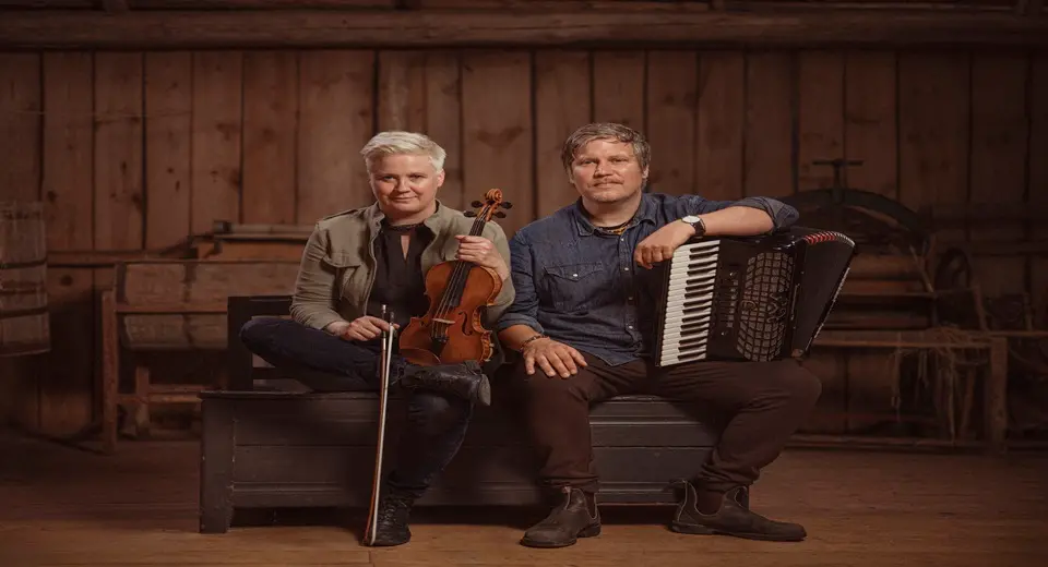 En man och en kvinna sitter med var sitt instrument i knät.