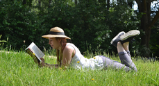 Kvinna i stråhatt läser bok i gräset