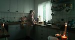 Äldre kvinna tittar ut genom fönstret i ett kök utan el